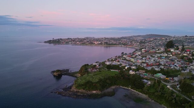 Chiloe Island, Chile: Dramatic aerial footage of sunset over Ancud, town in Chiloe Island in Lake District of Chile. Taken with upward and tilt down motion above the beach and residential area.