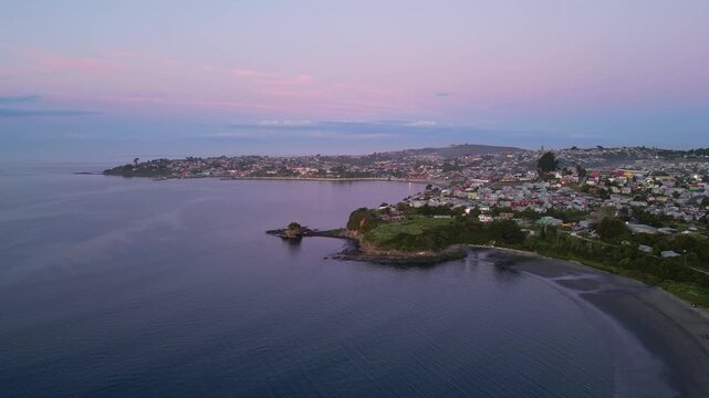 Chiloe Island, Chile: Dramatic aerial footage of sunset over Ancud housing areas, town in Chiloe Island in Lake District of Chile. Taken with forward and tilt down motion