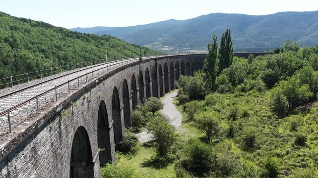 Historic stone railway viaduct arching over verdant valley, connecting mountainous landscape with elegant engineering marvel