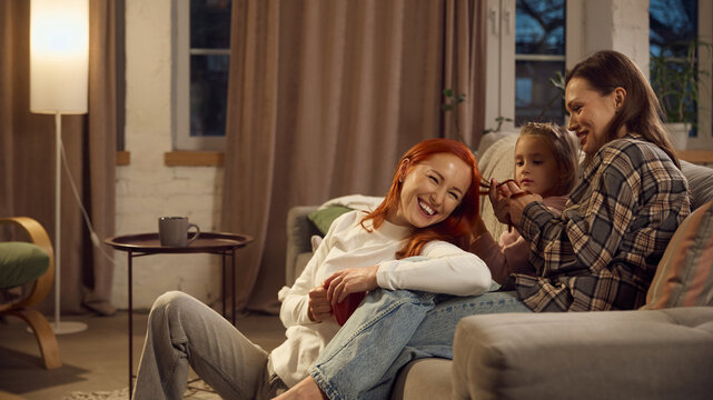 Warm evening conversation between women and child on sofa. Concept of supportive home environment, family unity, diversity inclusion materials, and emotional wellbeing content.