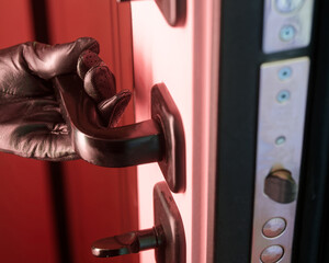 Hand in black leather glove opening armored door handle from inside with red light. Concept of illegal squatter, okupas, thief entering house, and anonymous criminal access. Photo
