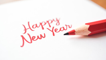 A red pencil writes happy New year on paper