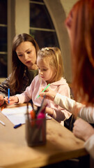 Woman guiding little girl during creative drawing session as second woman observes. Concept of...