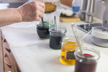 A close-up of the process of dyeing an Easter egg. The egg is being removed from the dye in a jar with a spoon. Other jars of dye are visible in the background