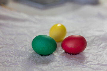 Brightly colored Easter eggs – various colors - green, yellow, red, blue – arranged on crumpled white paper. The eggs are smooth and shiny, ready for decoration or display at Easter
