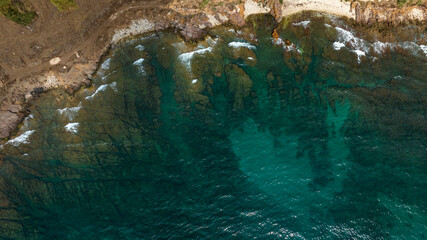 Aerial zenithal view of the rocky coast overlooking the crystal-clear turquoise sea. Holiday concept.