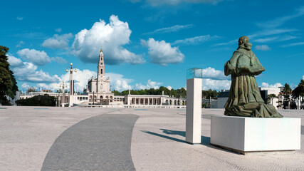 Bronze statue of Pope Paul VI, praying, kneeling with weathered green patina stands before Basilica of Our Lady of the Rosary at Sanctuary of F&aacute;tima, Portugal, iconic religious monument under blue sky
