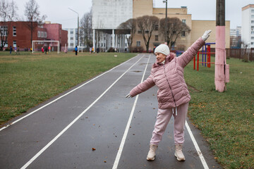 78-year-old pensioner doing exercises side bends at stadium. Senior woman practice sports outdoors. Retiree healthy lifestyle, outdoor physical activity in city.