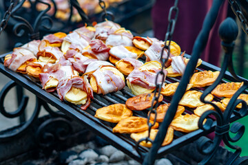 Grilled oscypek cheese wrapped in bacon resting on a cast-iron grate creates an aromatic culinary Christmas market scene in Poznań