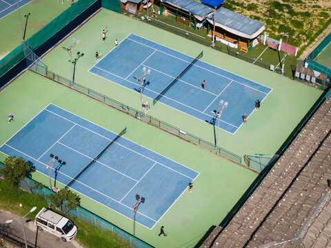 Aerial view of blue tennis courts with white lines sharply contrast against the green surroundings, showcasing players in action, Thimphu, Bhutan.