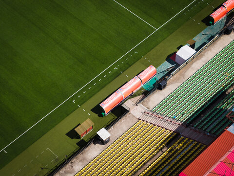 Aerial view of vibrant stadium seats in hues of yellow and green adjacent to a perfectly manicured green football field, Thimphu, Bhutan.