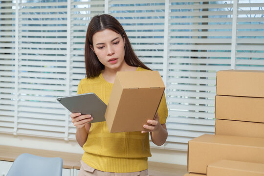 Asian female entrepreneur holding parcel using tablet analyzing delivery information startup e-commerce business concept of technology management and success in digital online retail office