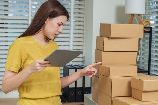 Asian woman business owner using tablet verifying order information checking stacked boxes in modern office concept of e-commerce logistics entrepreneur technology and online retail management