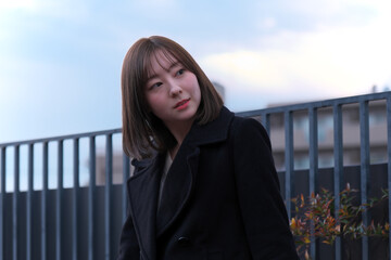 Obraz premium 【都会の冬のポートレート】アンニュイな表情で遠くを見つめる日本人女性の横顔 - 夕暮れの屋上テラスと黒いコート