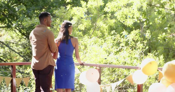 Couple walking onto deck past balloons pausing at railing man placing hand taking view during party