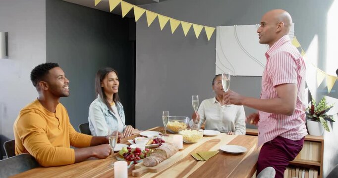 Four adults celebrating at dining table man speaking then rising toasting as ring overlay clearing