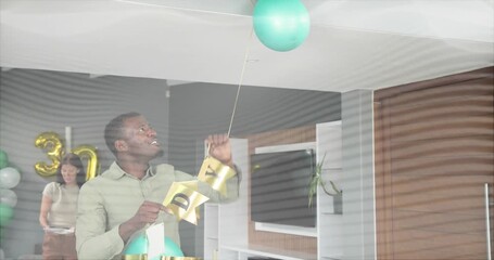 Man entering home holding teal gold balloons and reaching up, adjusting banner for 30th birthday
