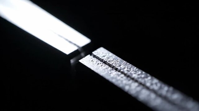 Close-up of a shiny metal zipper on a dark background, reflecting light and creating a striking visual effect.