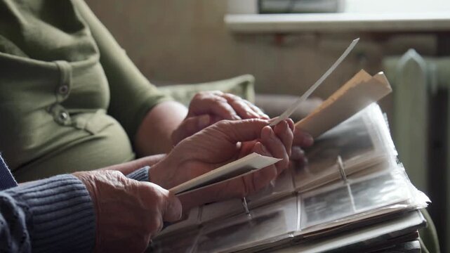 Seniors fondly viewing photographs. Wrinkled fingers gently turning pages of treasured keepsake album. Two aged adults sharing nostalgic moments as they explore their old picture collection together