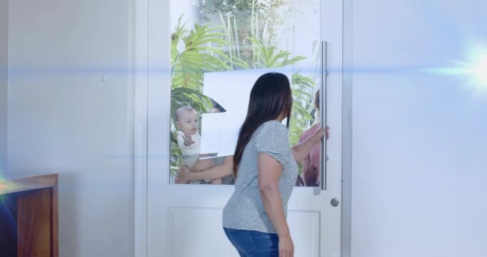 Host opening glass-panel door, welcoming guests with baby, plants framing entry for home marketing