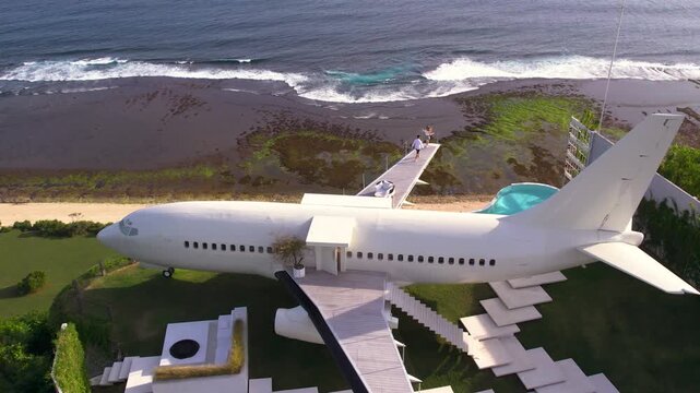 Luxury hotel made from airplane in Bali, beachfront villa with ocean view. People walk on the wing of aircraft. Honeymoon vacation of couple
