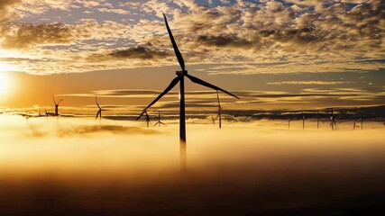 Wind turbines stand tall amidst a calm, fog-covered landscape during a stunning sunrise. the vibrant sky and misty surroundings emphasize the concept of renewable energy and sustainability in a tranqu - Powered by Adobe