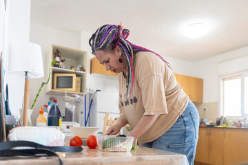 Focused mature woman with dreadlocks and curvy body preparing healthy meal in kitchen