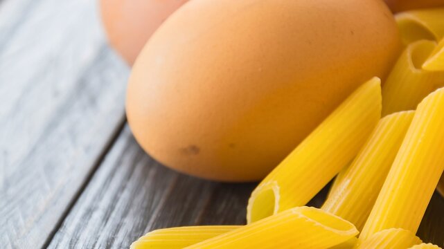Fresh eggs and penne pasta on a wooden surface - Powered by Adobe