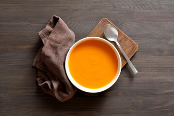 Delicious pumpkin and carrot soup on brown wooden background.