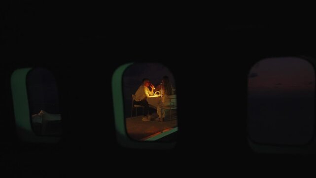 Romantic dinner with candles served in the restaurant of unique villa in Bali made from the aircraft, shot from the illuminator window. Couple have date at night at the VIP luxury hotel airplane style