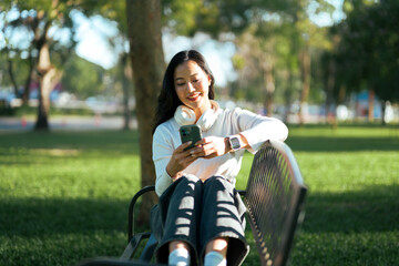 Smiling asian woman using smartphone on park bench