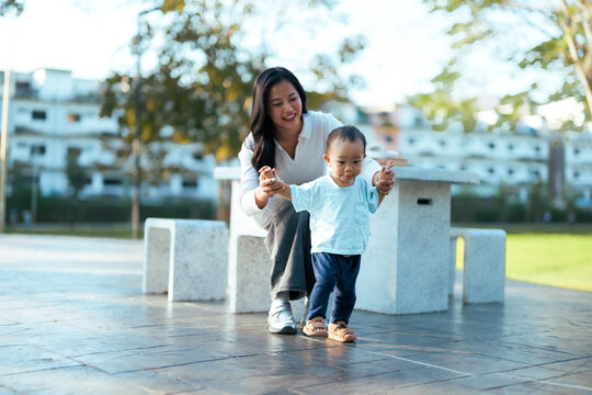 Mother supporting toddler learning first steps in park