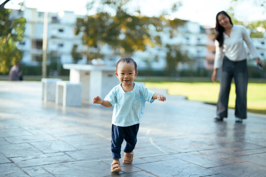 Asian toddler learning to walk outdoors with mother - Powered by Adobe