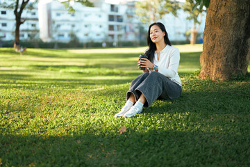 Woman sitting on grass relaxing with coffee in park