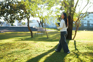 Young woman student walking on campus park with books