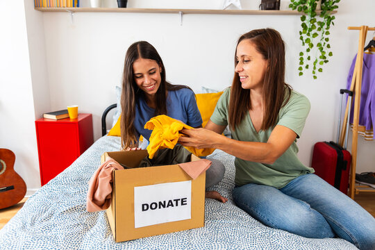 Cheerful Caucasian mother and daughter organizing clothes for donation on the bed. Concept of generosity, unity, and positive lifestyle.