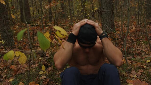 Shirtless bodybuilder training in an autumn forest and does crunches while lying down in glade covered with yellow leaves.