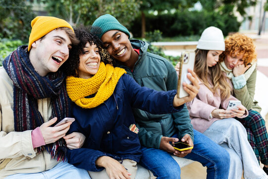 Happy young students using smartphones at city street on winter. Social media and technology lifestyle concept