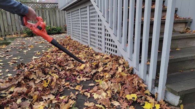 A gardener in denim jacket using an orange battery powered leaf blower (no brand labels) with sound
