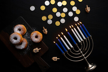 A Hanukkah celebration flat lay with a lit menorah, donuts, and gelt on a dark, festive background.