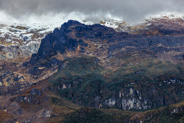 Detalle del Nevado del Ruiz, Colombia: picos montañosos, roca volcánica oscura, vegetación de alta montaña y nieve remanente bajo una densa capa de nubes, paisaje andino.