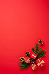 A simple Christmas flat lay with a corner border of red gift boxes and fir branches on a red background.