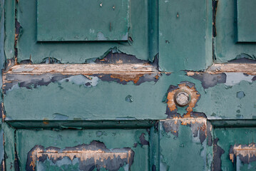 A close-up of a weathered teal door with peeling paint and a round knob, revealing aged wood and rustic character. Rustic vintage texture