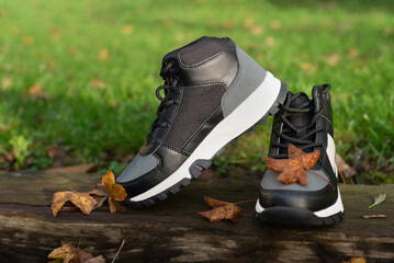 Casual black and gray sneakers rest on weathered wooden surface with autumn leaves nearby, conveying outdoor activity, style, and seasonal warmth. Modern waterproof high shoes for winter
