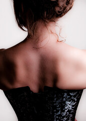 A woman's back and shoulders are shown, wearing a black corset.