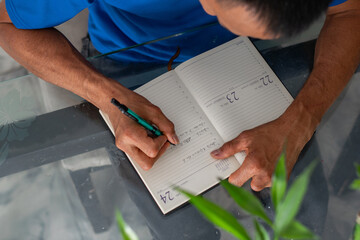 Overhead shot of man writing in notebook with both hands visible, left hand missing four fingers, organizing day