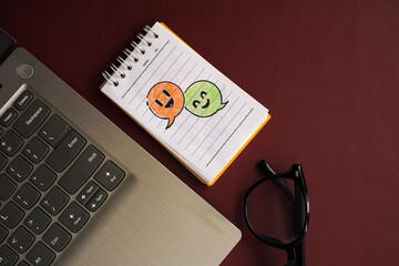 Top view of a notebook with hand-drawn conversation bubbles beside a laptop and glasses on a dark background with copy space, symbolizing online communication and social media