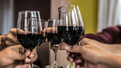 Close-up of a toast with four hands raising wine glasses. Intense colors.