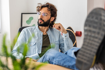 Portrait of young business man looking away while relaxing at home office workplace