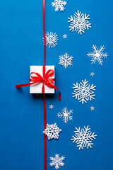 A modern Christmas flat lay with a small white gift and paper snowflakes on a blue background.